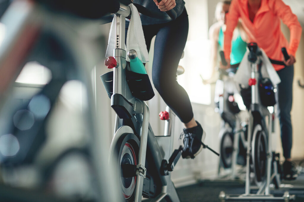 Fitness, legs and exercise bike with people in a gym for a cardio or endurance spinning class workout. Health, wellness and energy with a sporty athlete group training or cycling in a sports center