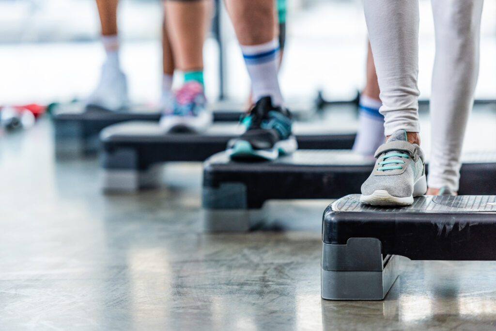 Cropped shot of sportspeople doing exercise on step platforms at gym